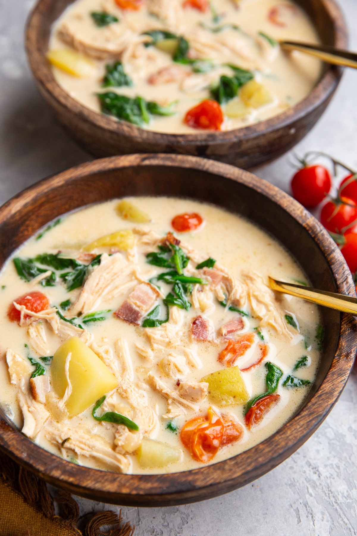 Two big wood bowls of creamy soup with golden spoons for eating.