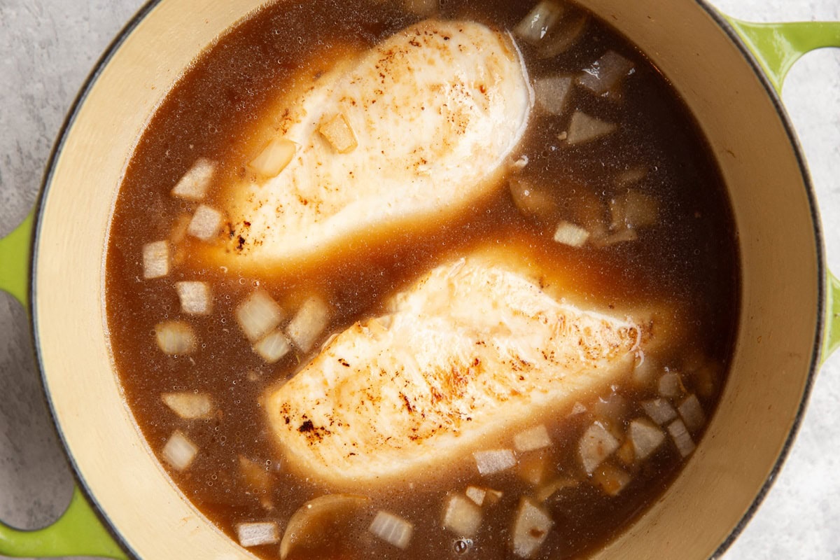 Broth, chicken, and onions cooking in a large soup pot.