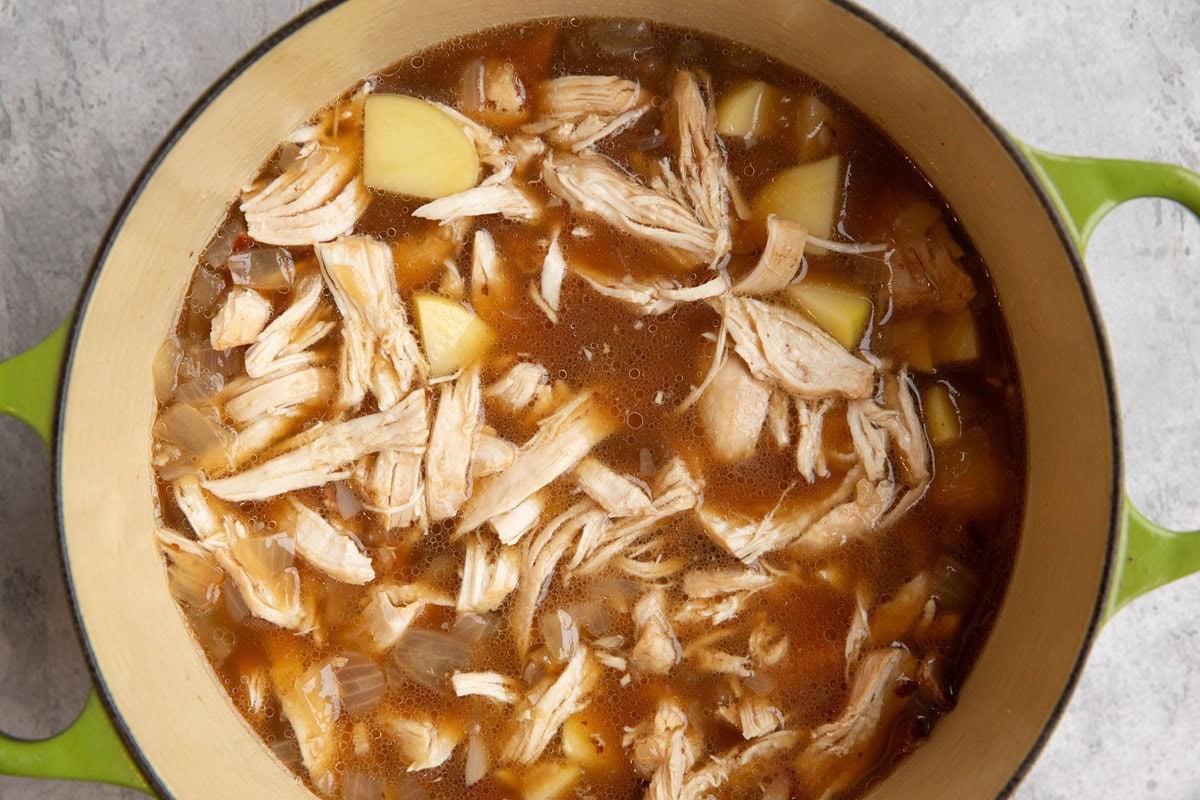 Pot of shredded chicken, potatoes, broth, and onion.