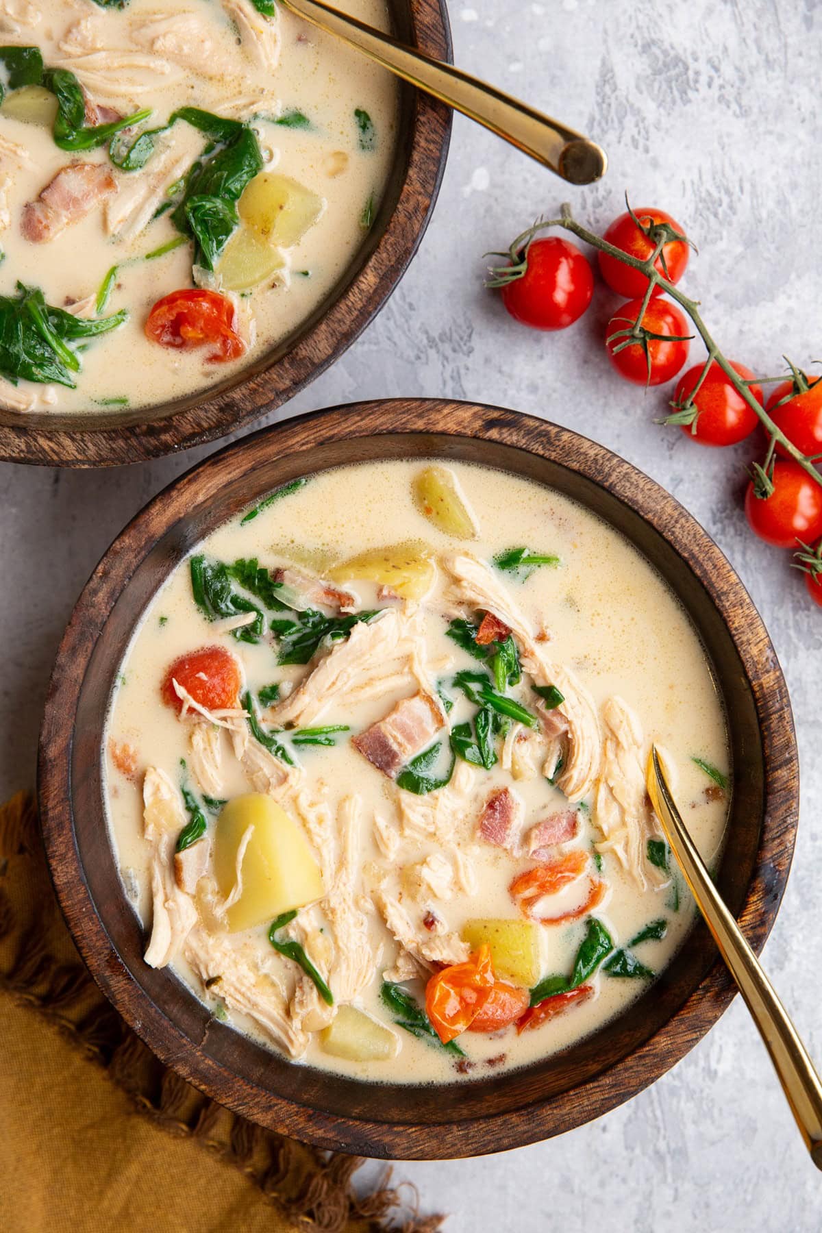 Two bowls of creamy soup with fresh tomatoes to the side and golden spoons