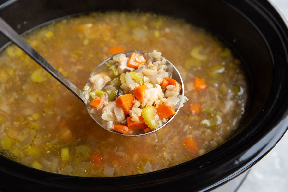 Slow cooker with a ladle taking out a scoop of soup.