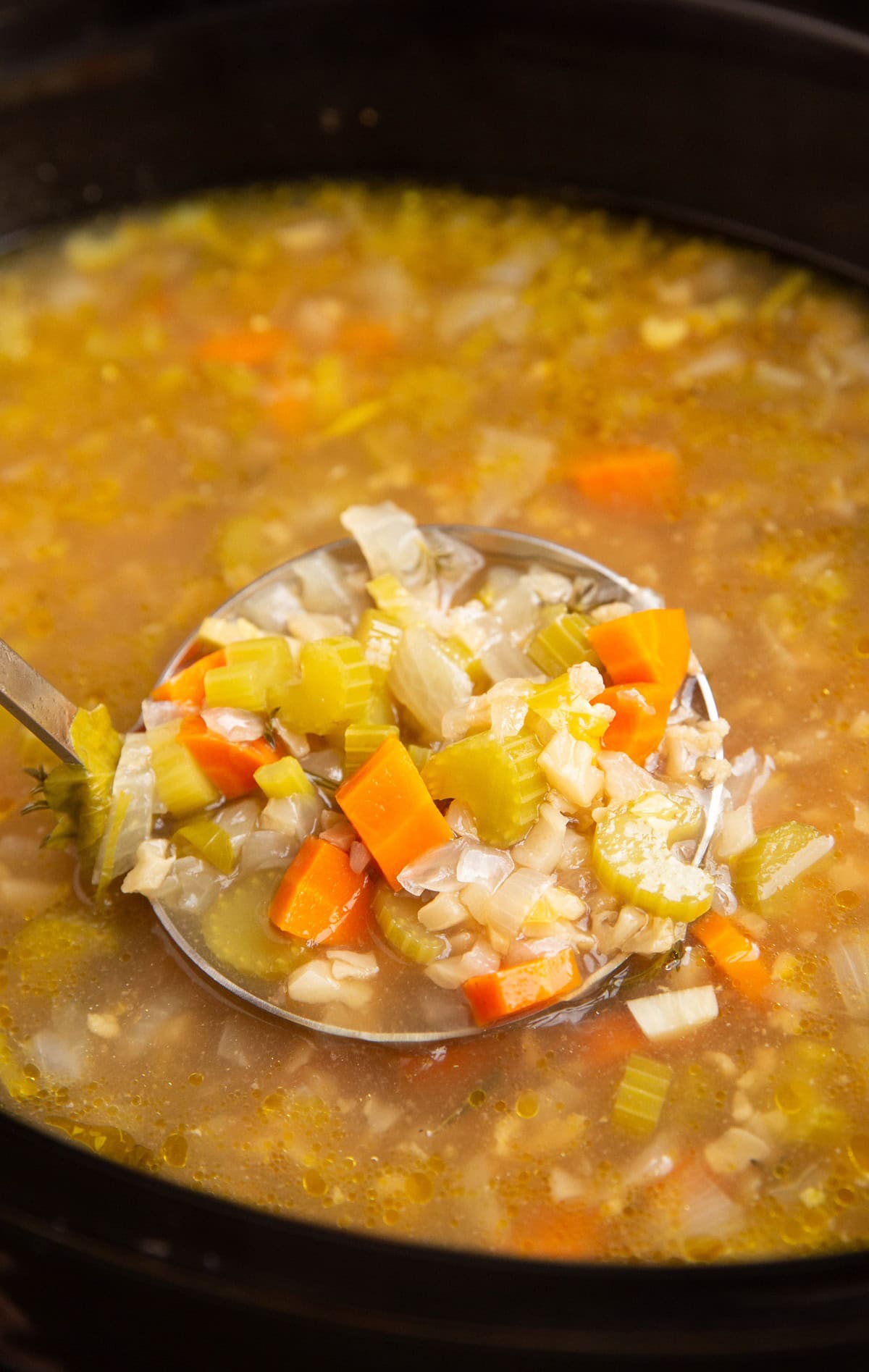 Big crock pot full of soup with a ladle scooping some of it out.