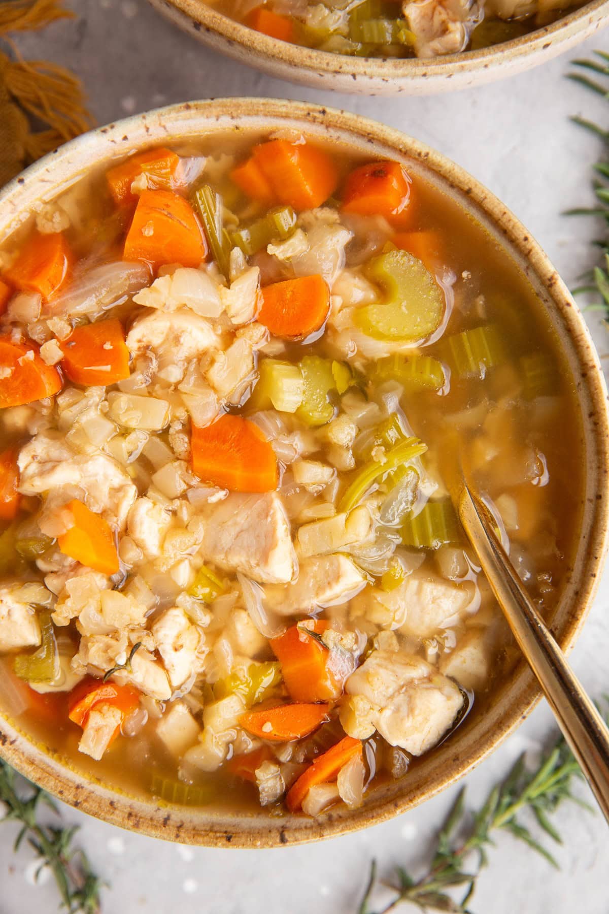 Two bowls of chicken and cauliflower rice soup with fresh sprigs of rosemary around.