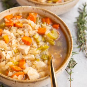 Two bowls of chicken cauliflower rice soup with gold spoons, ready to serve.