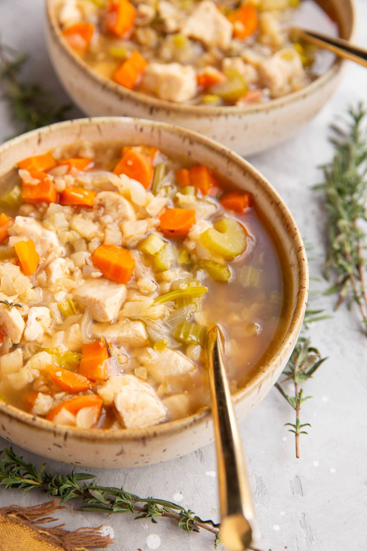 Two bowls of chicken cauliflower rice soup with gold spoons, ready to serve.