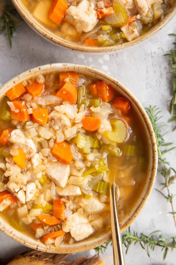 Two bowls of chicken and cauliflower rice soup with gold spoons.