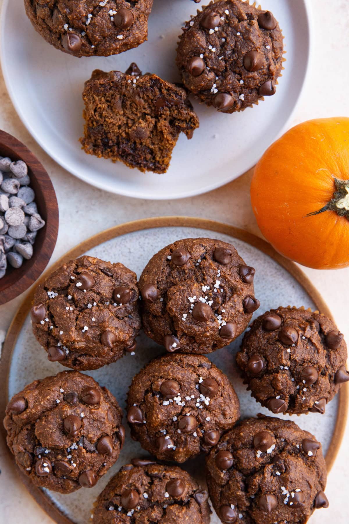 Two plates of pumpkin chocolate muffins with one sliced in half to expose the inside.