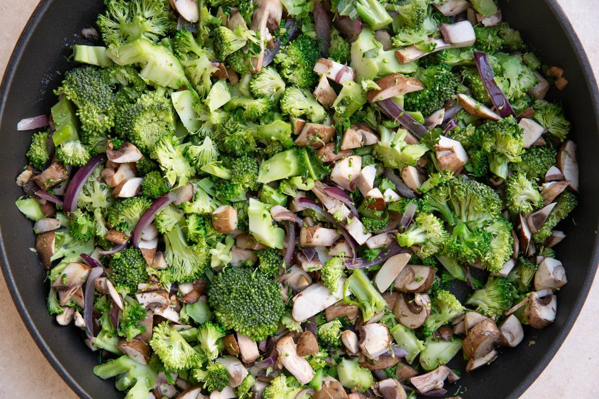 Raw broccoli, mushrooms and onions in a skillet