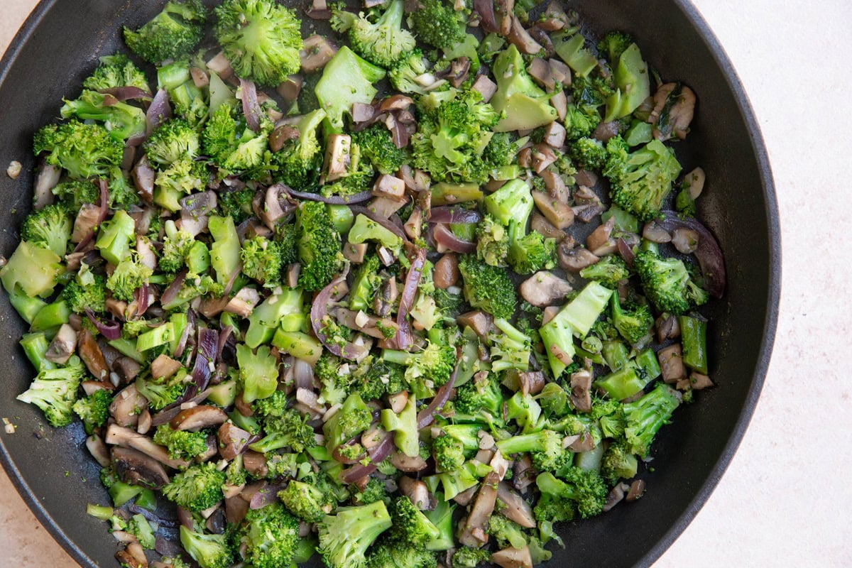 Broccoli, mushrooms and onions cooking in a skillet.