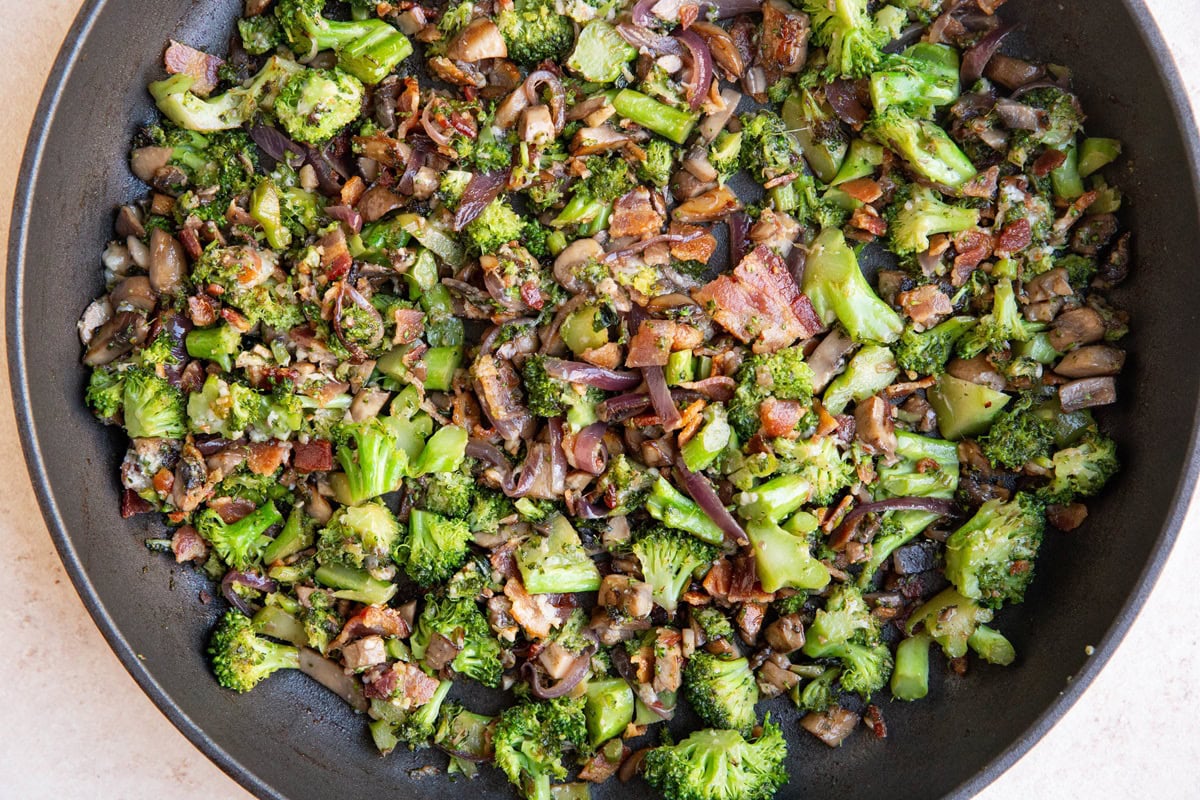 Skillet full of sauteed broccoli and mushrooms with bacon.