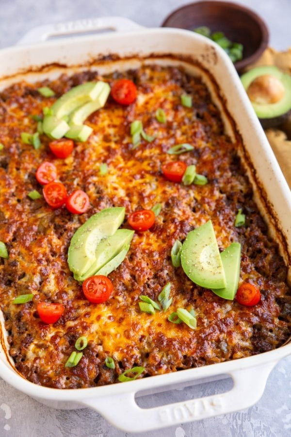 Casserole dish full of cheesy enchilada casserole topped with avocado and tomatoes