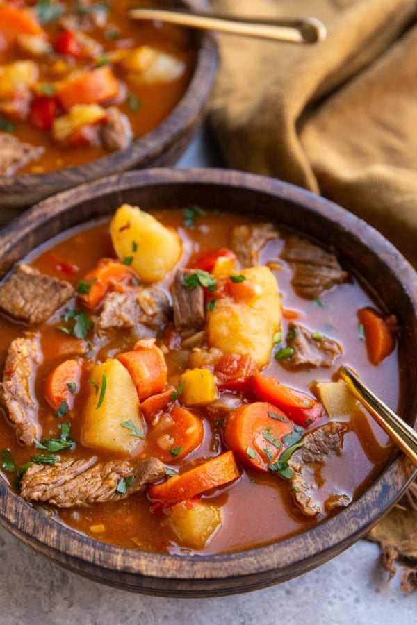 Two wooden bowls of goulash with a gold spoon, ready to eat