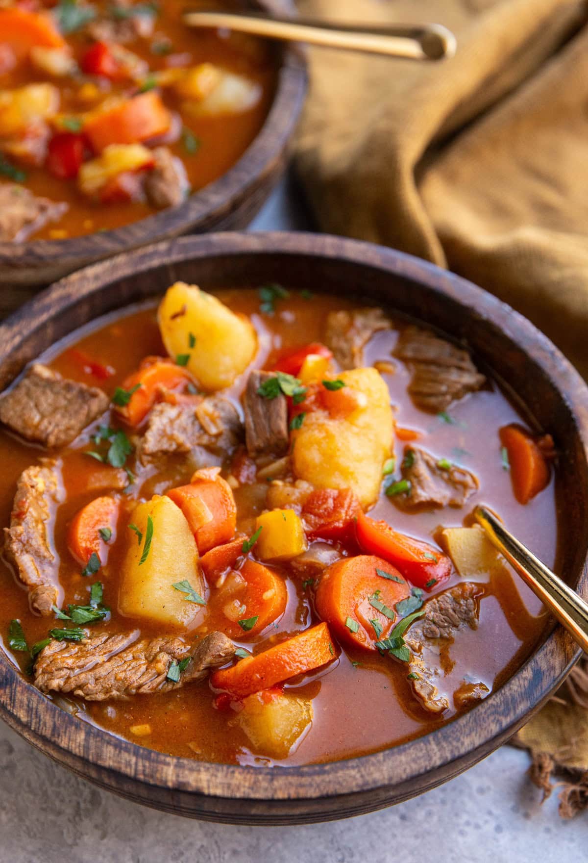 Two wooden bowls of goulash with a gold spoon, ready to eat