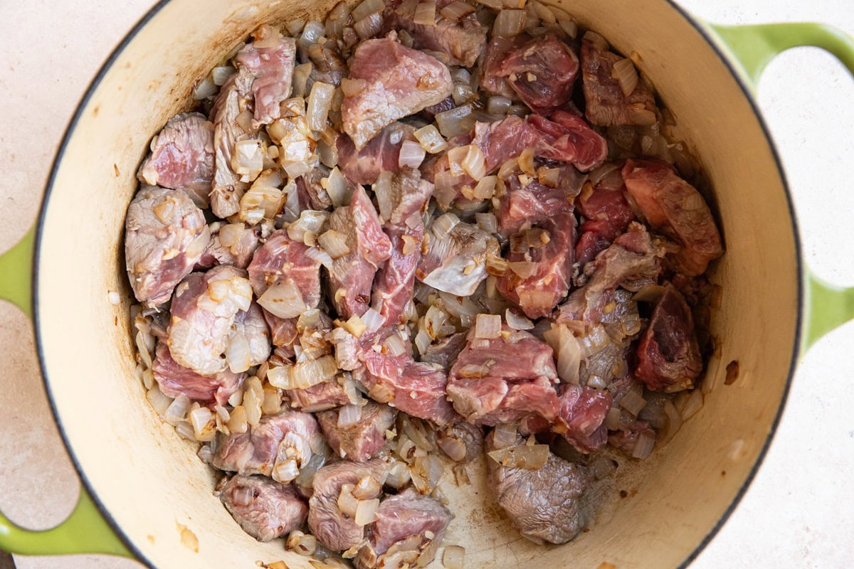 Beef browning in a large Dutch oven with onions and garlic