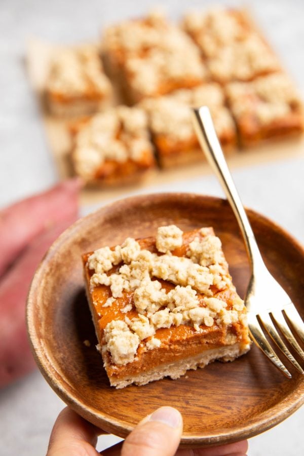 Hand holding a plate with a sweet potato bar and a fork.