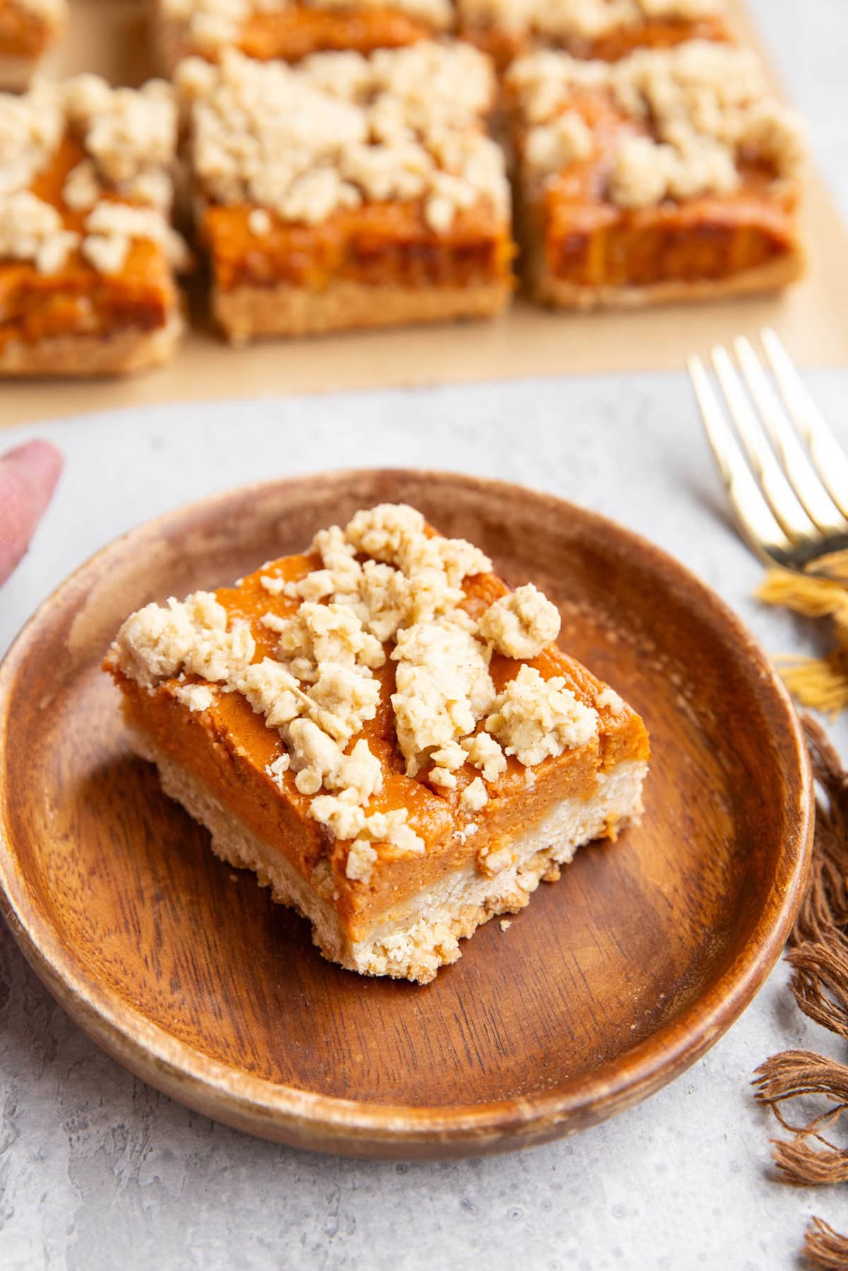 Sweet potato pie bar on a wooden plate with the rest of the bars in the background.