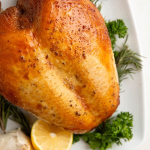 Whole turkey breast on a platter with fresh herbs and lemons.