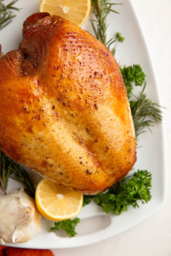 Whole turkey breast on a platter with fresh herbs and lemons.