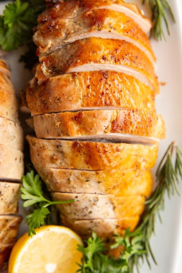 Turkey breast cut into slices with fresh herbs and lemon around, ready to serve.