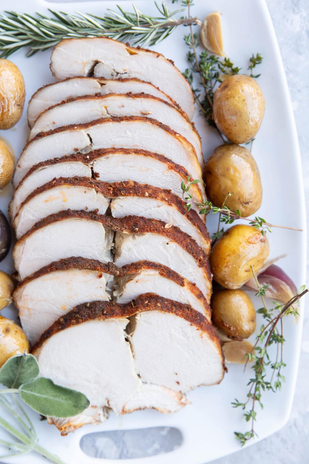 Platter of sliced turkey meat with potatoes and fresh herbs all around.