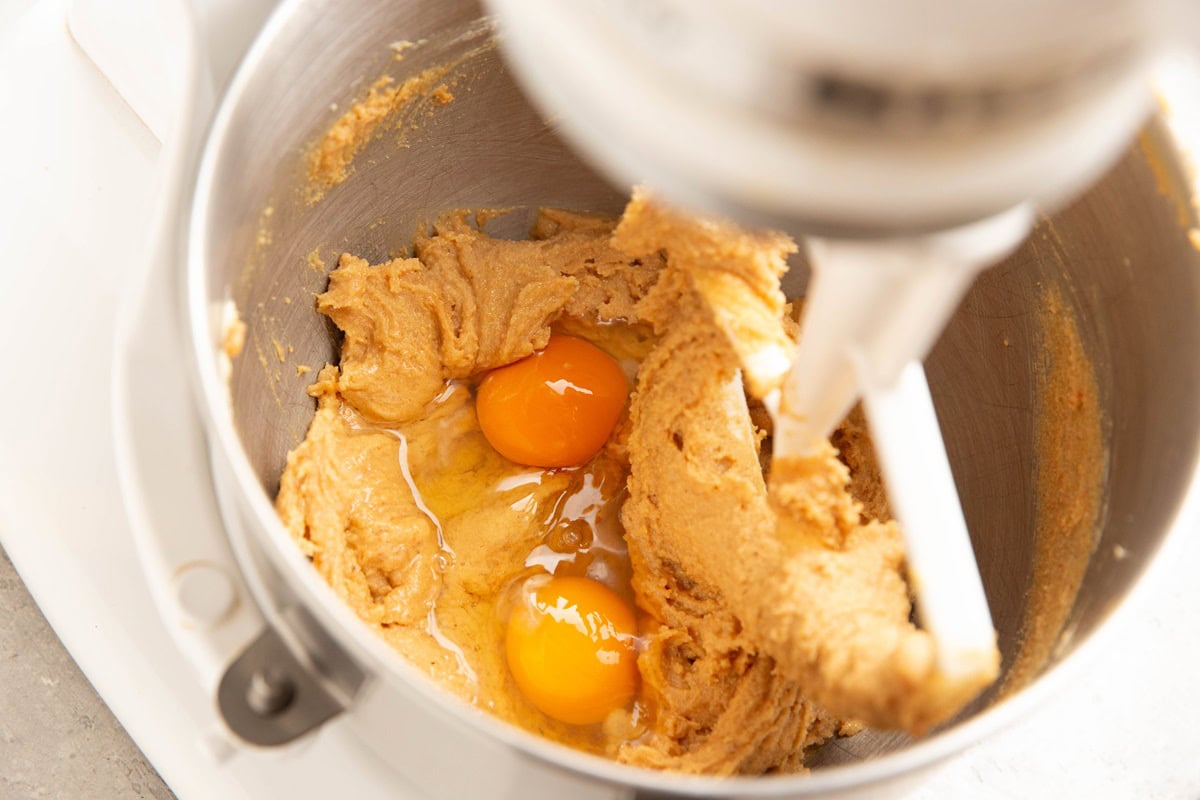 Stand mixer with butter, peanut butter, and sugar mixed together with eggs inside the mixer to be mixed in.