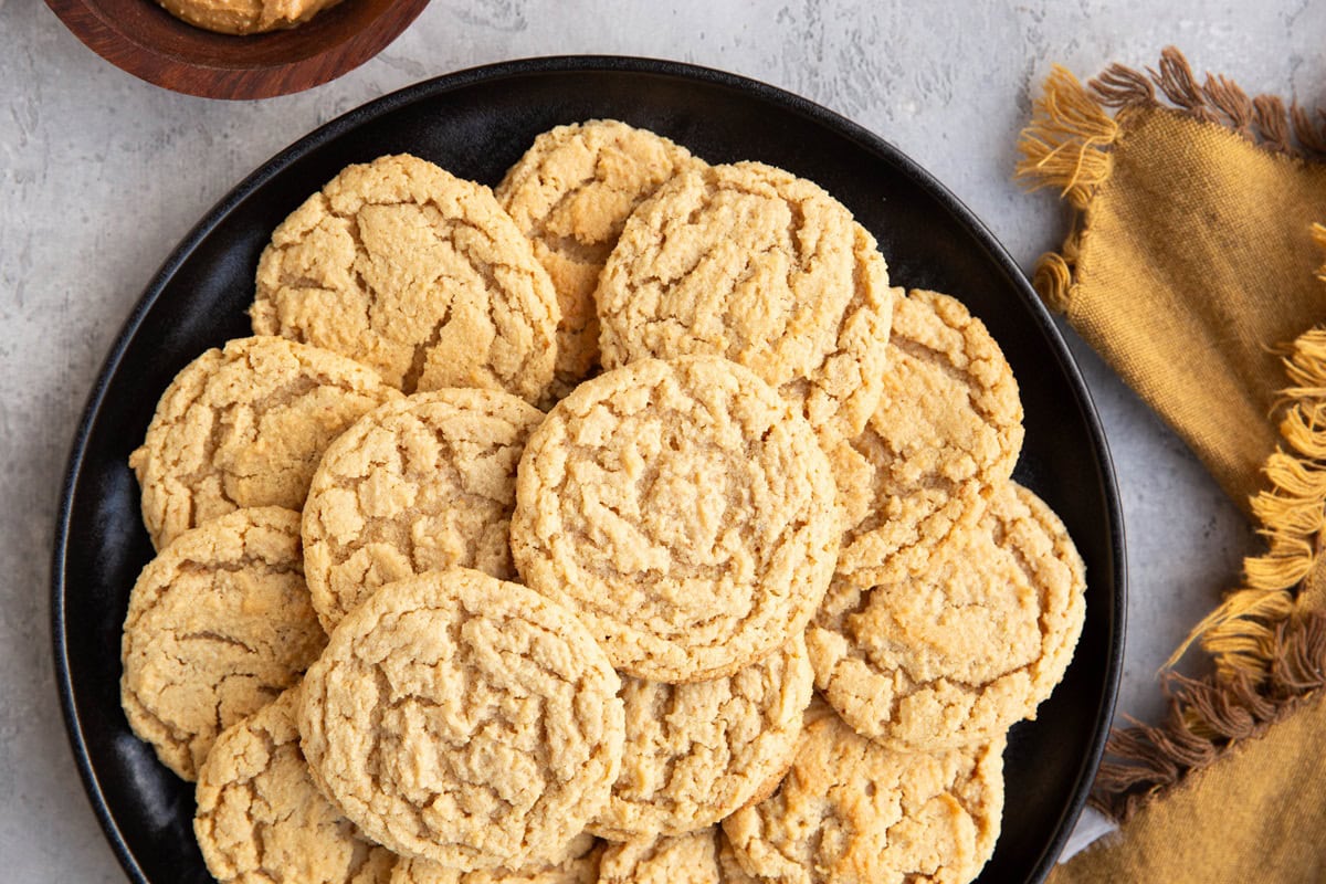 Black plate of peanut butter cookies with a gold napkin to the side, ready to serve.