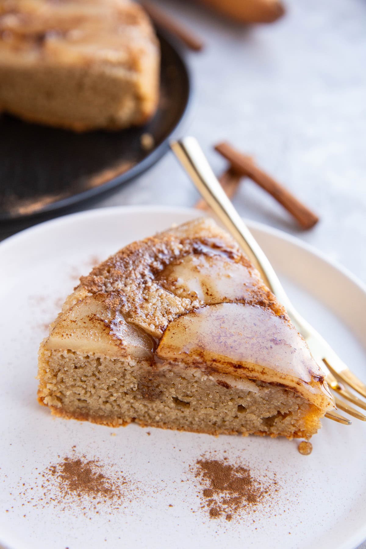 White plate of slice of pear cake with a golden fork.