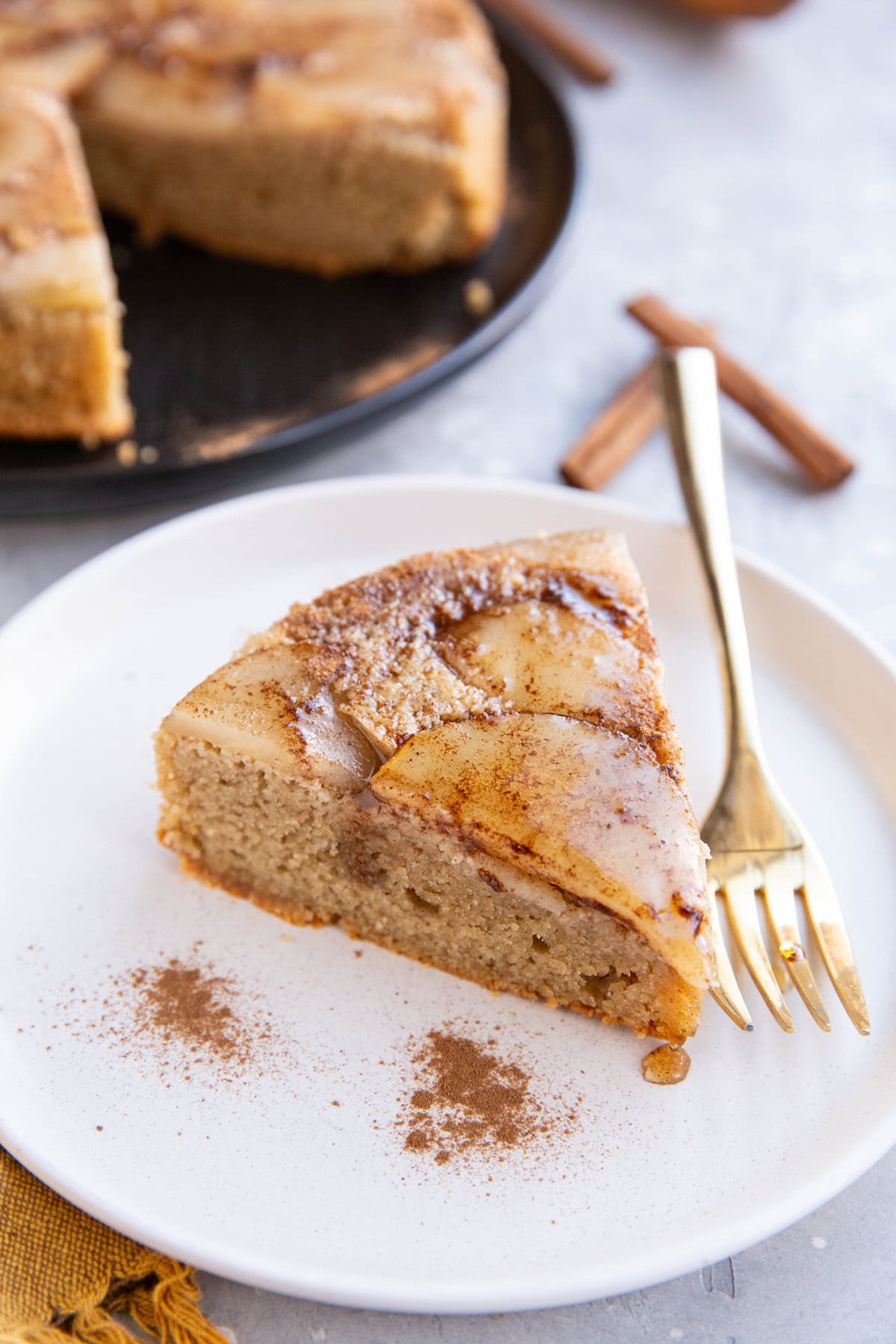 Slice of pear cake on a white plate with gold fork and cake in the background.