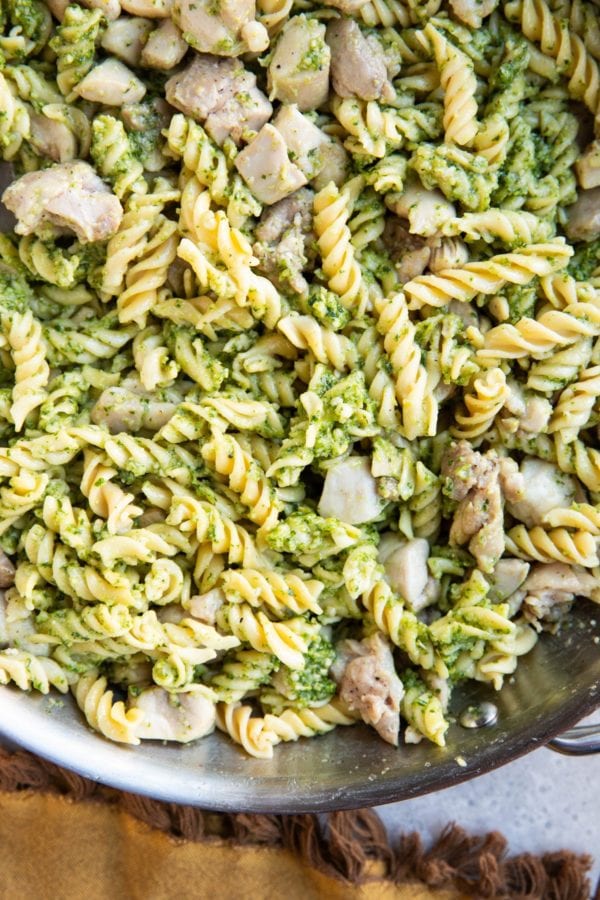 Stainless steel skillet of chicken pesto pasta with a napkin.