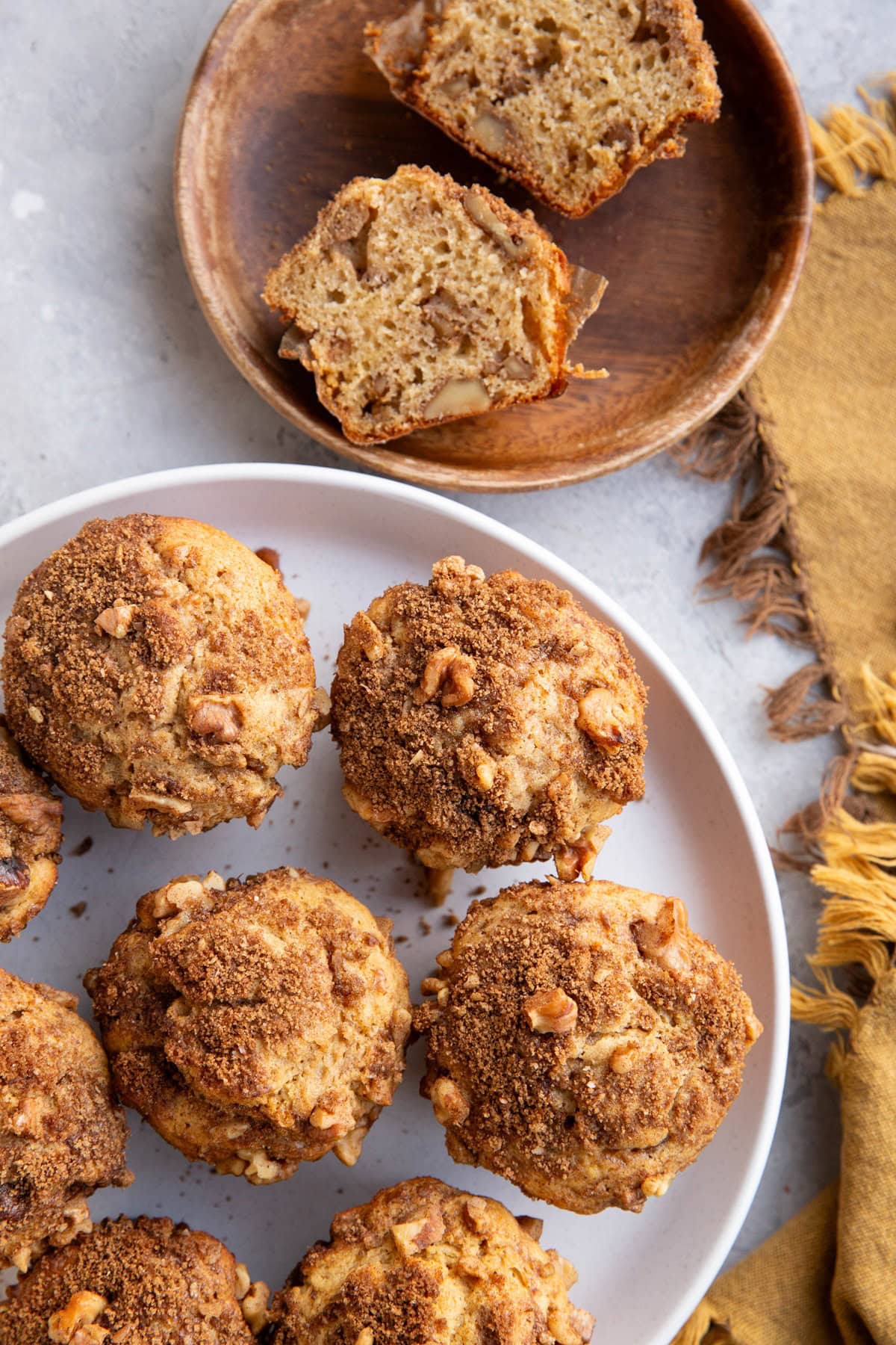 Coffee cake muffins on a large white plate with one cut in half on a separate plate to expose the center,