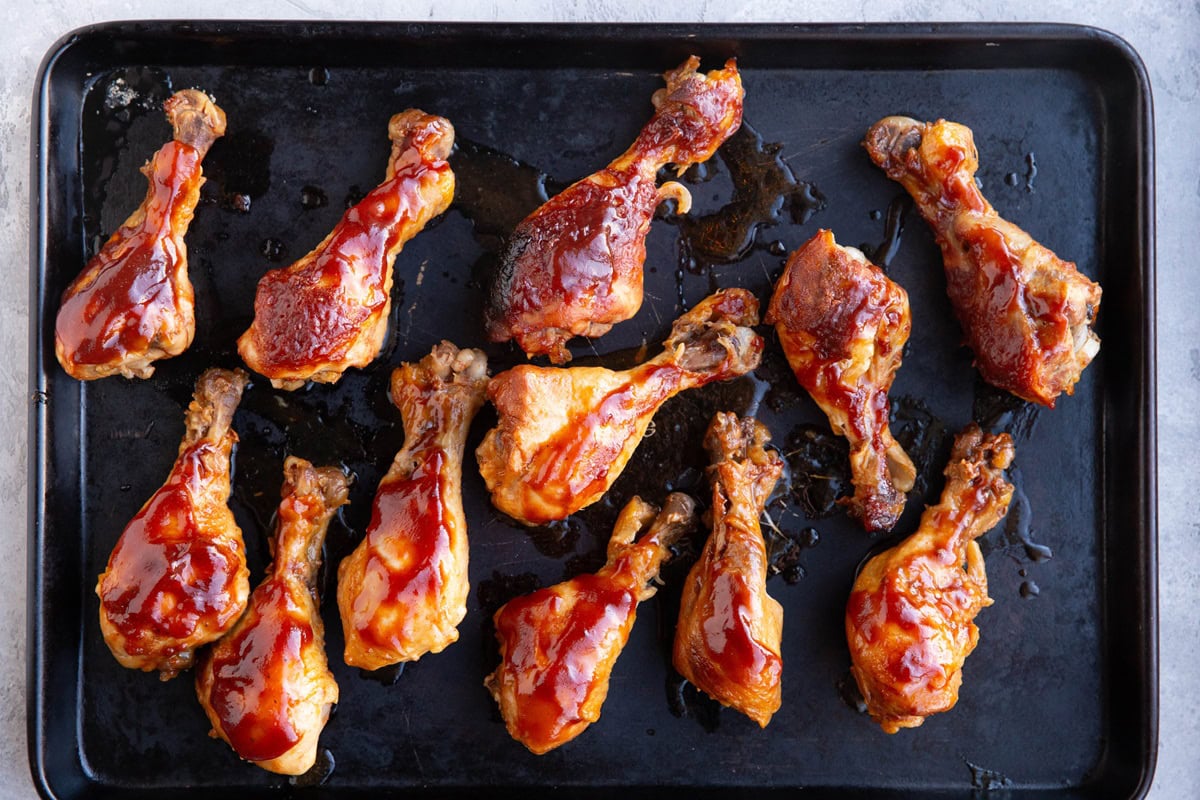 Sheet pan with chicken drumsticks with bbq sauce on top.