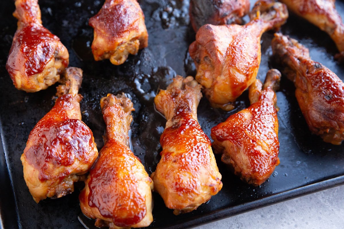 Sheet pan of chicken drumsticks covered in bbq sauce, ready to serve.