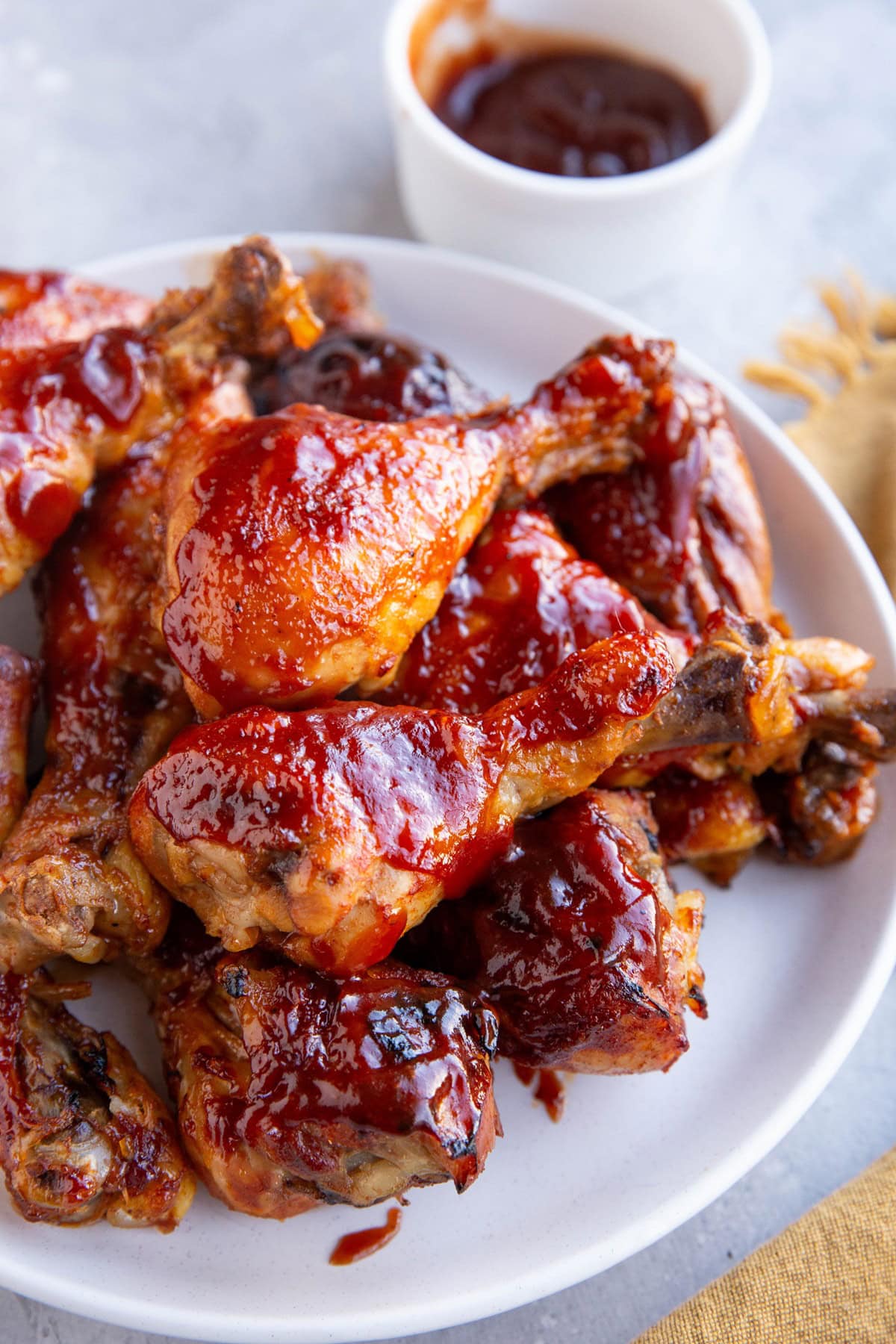 White plate full of chicken drumsticks coated with bbq sauce.