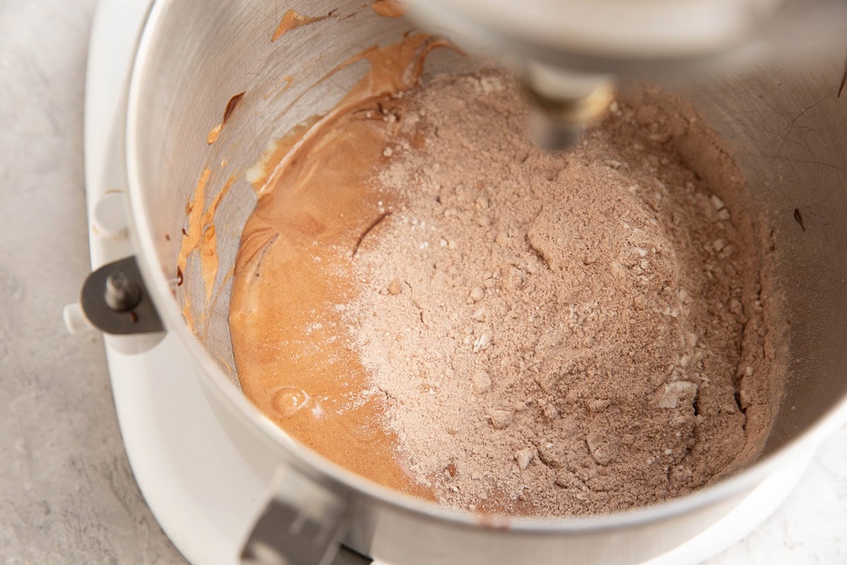 Stand mixer with wet ingredients and dry ingredients on top, ready to be mixed in.