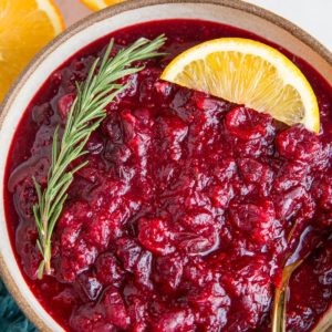 Orange ginger cranberry sauce in a bowl with fresh oranges and a blue napkin to the side.