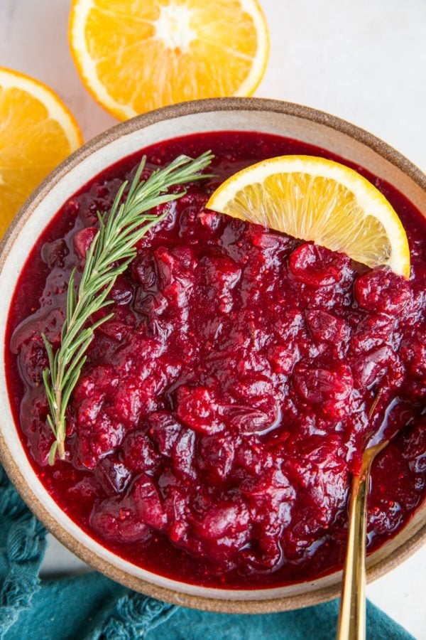 Orange ginger cranberry sauce in a bowl with fresh oranges and a blue napkin to the side.