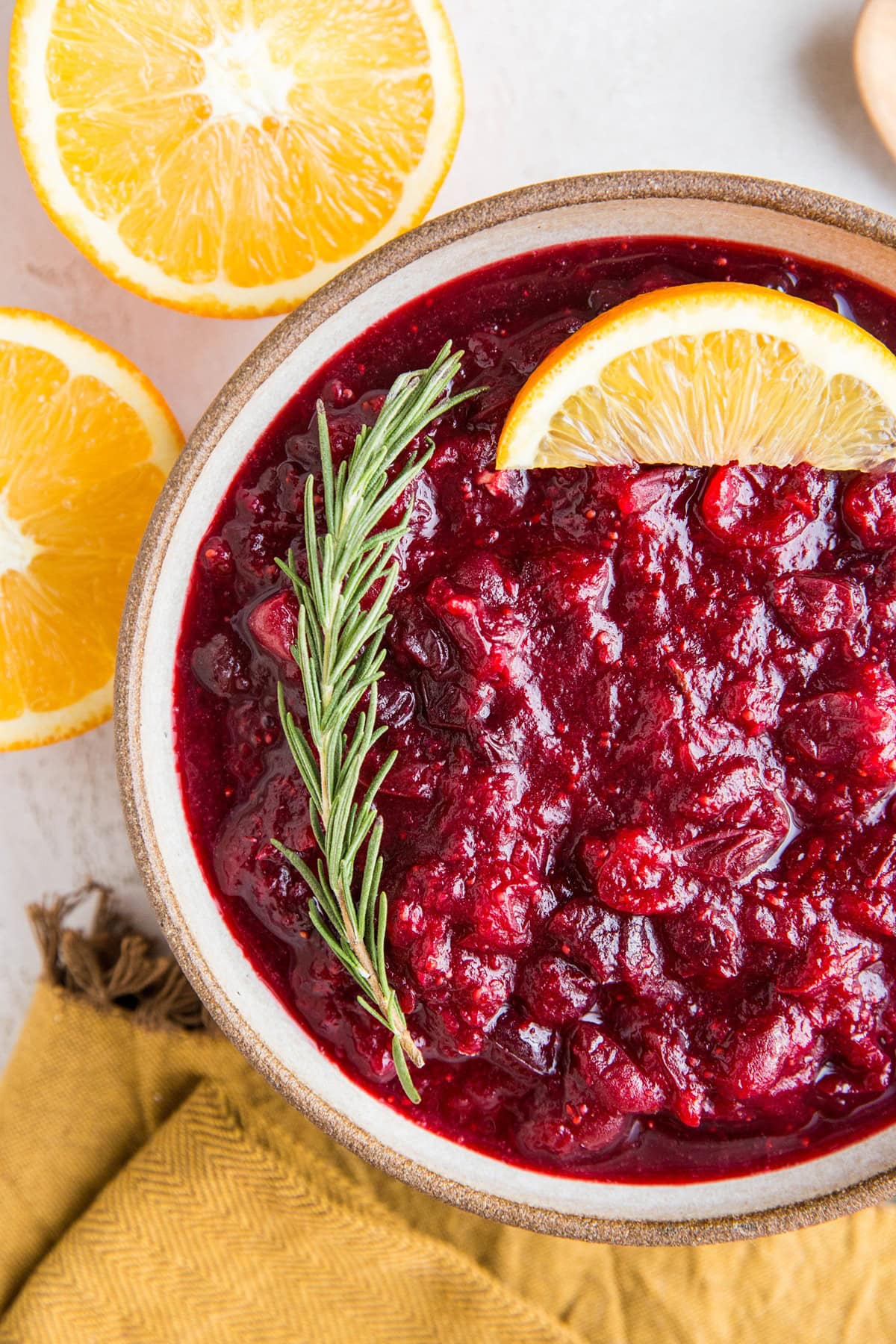 Ginger orange cranberry sauce in a bowl with a fresh sprig of rosemary and fresh oranges to the side.