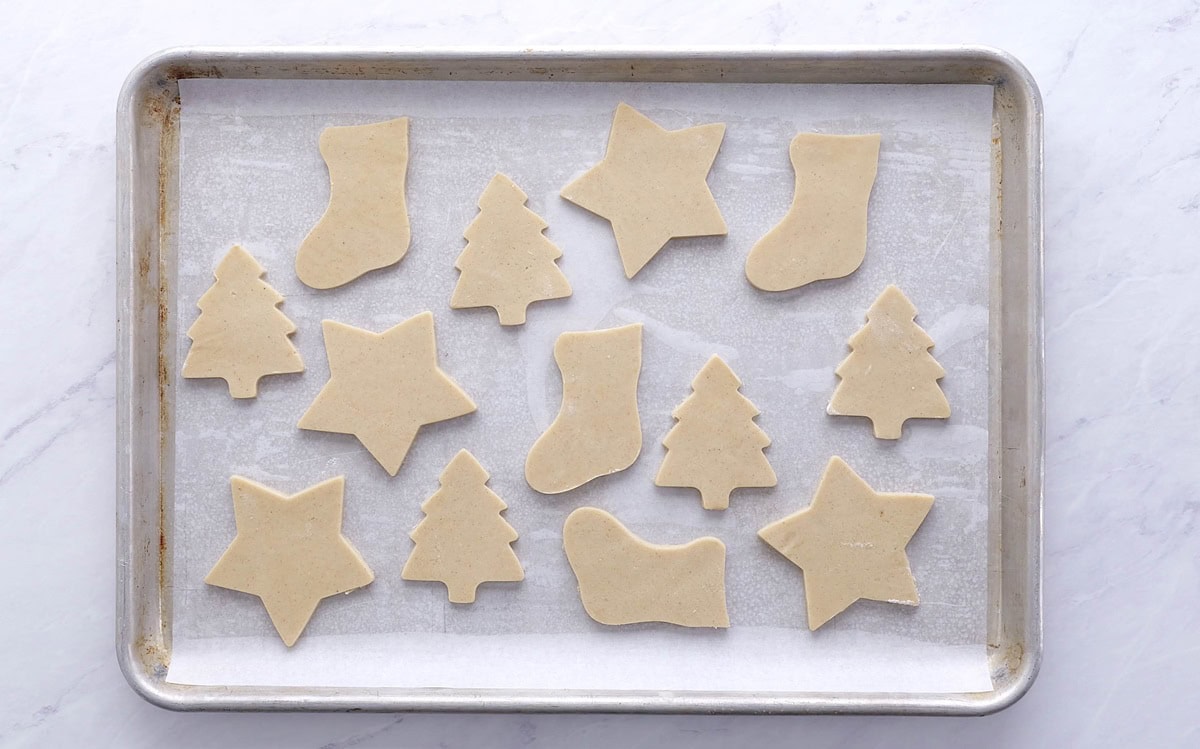 Baking sheet with parchment paper and cookie cut out shapes to make sugar cookies.