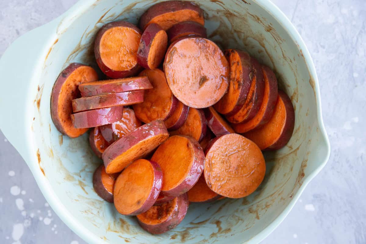 Mixing bowl with sweet potato slices covered in butter and cinnamon