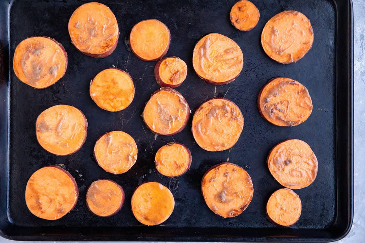 Slices of sweet potatoes on a large rimmed baking dish, ready to go into the oven.