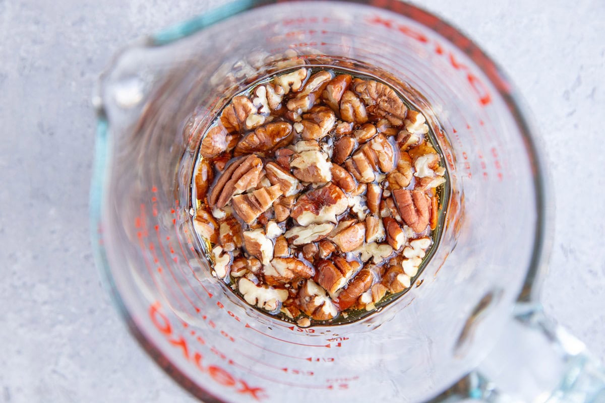 Maple syrup and chopped pecans in a mixing bowl, to be used on top of melting potatoes.