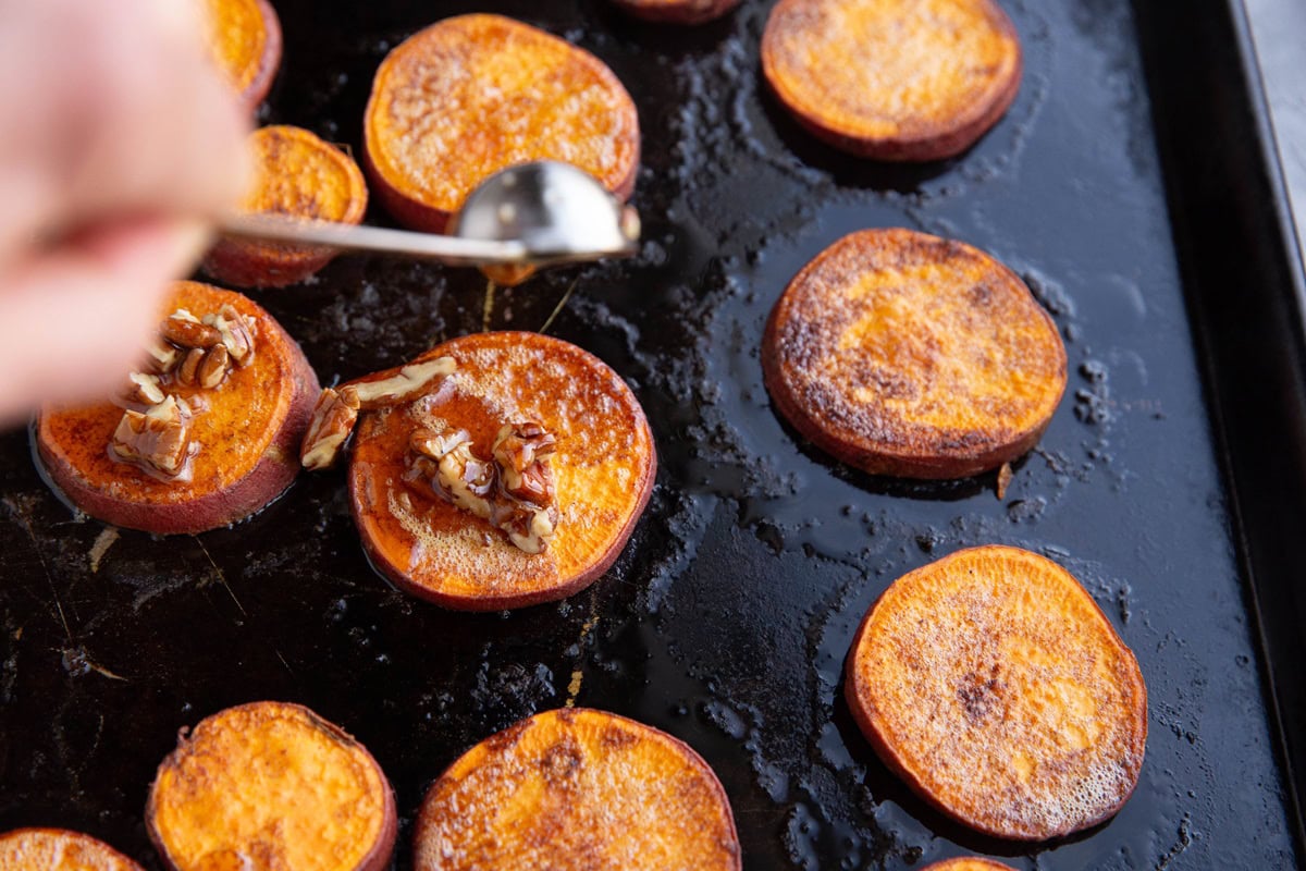 Hand pouring pure maple syrup and pecans over melting potatoes.