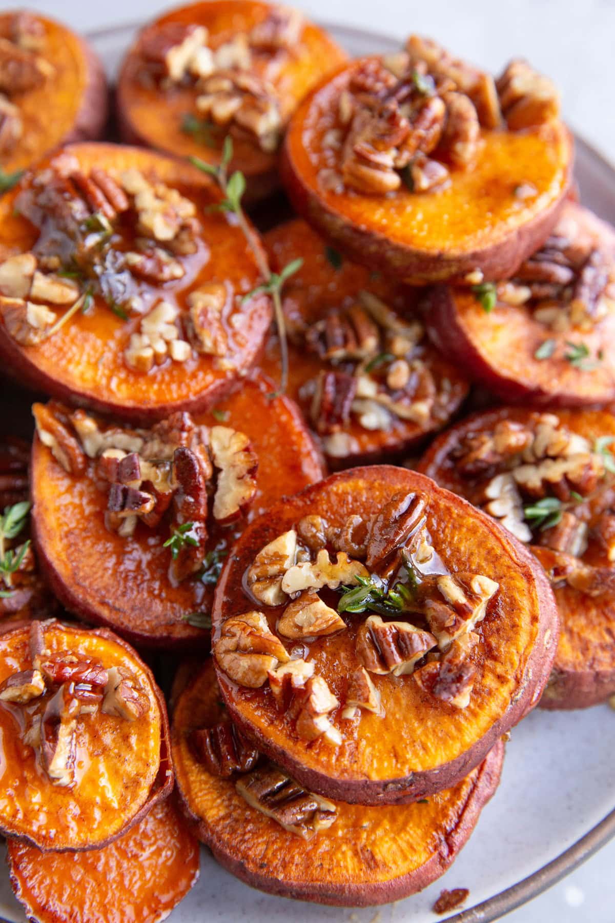 Large plate of sweet potato slices covered with pecans and thyme.