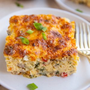 Large slice of cottage cheese egg bake on a white plate with a golden fork, ready to eat.