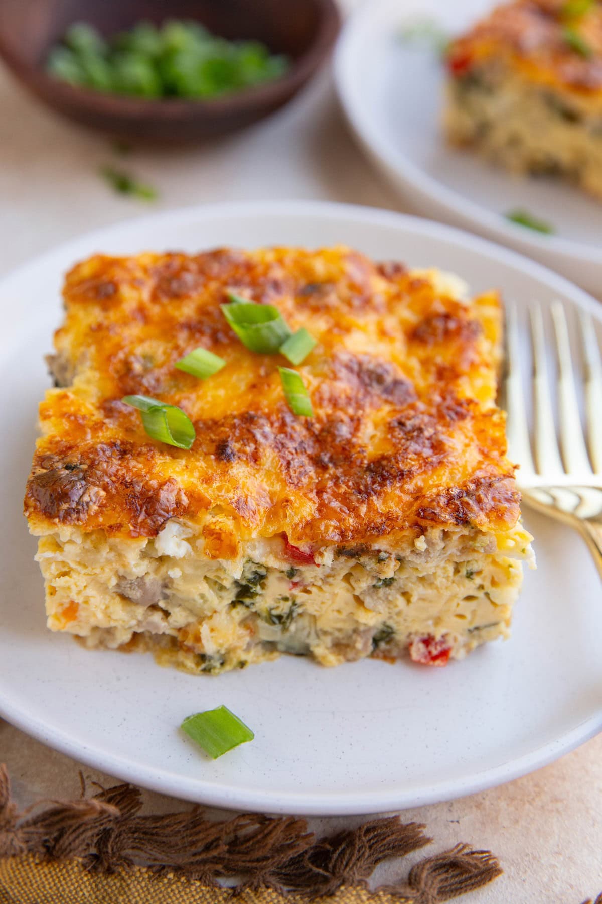 Large slice of cottage cheese egg bake on a white plate with a golden fork, ready to eat.