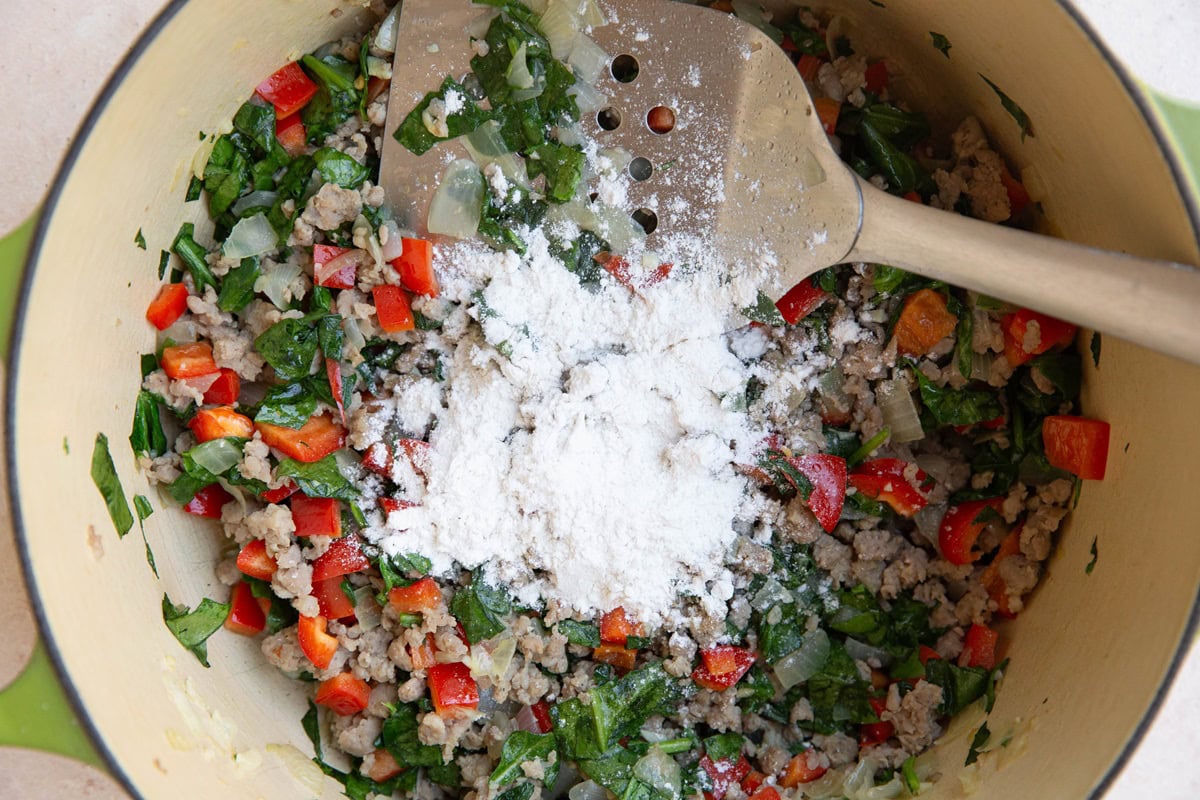 large pot of sausage and vegetables with flour sprinkled on top.