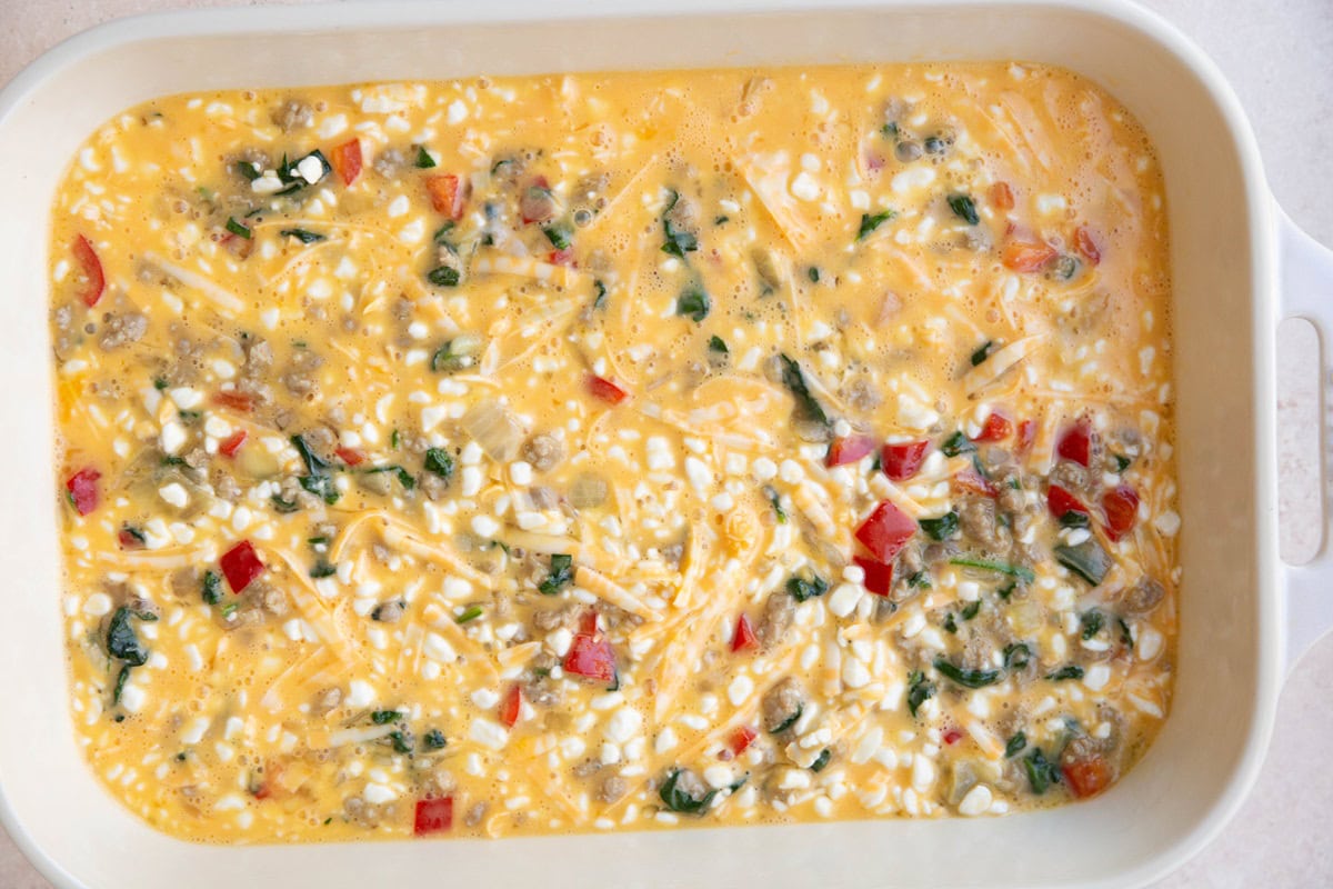 Casserole dish full of egg and cottage cheese mixture with meat and veggies.