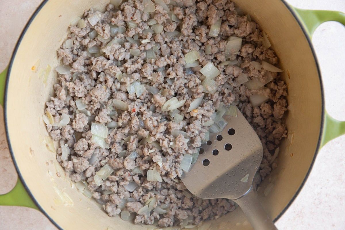 Sausage and onions cooking in a large pot.