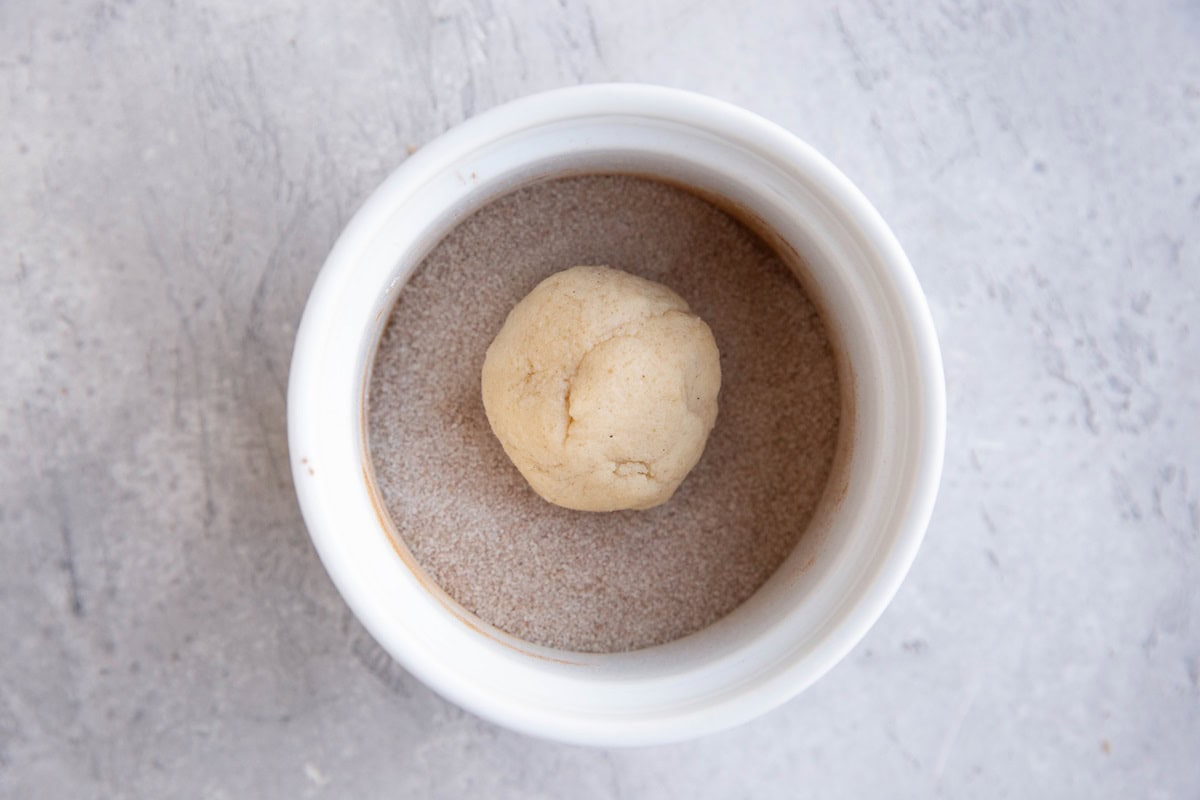 Cookie dough ball in a small bowl with cinnamon and sugar, ready to be rolled.