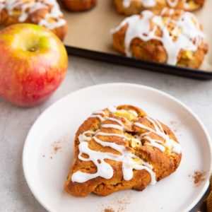 Plate with an apple scone on it with the baking sheet of scones in the background.